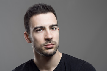 Close up moody portrait of skeptical stubble man looking at camera over dark gray studio background.