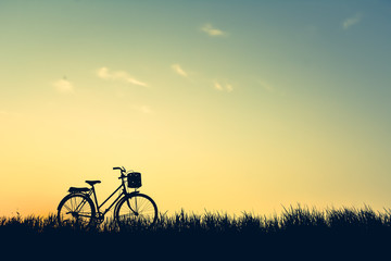 Obraz premium Silhouette of old bicycle on grass with the sky sunset, color of vintage tone and soft focus concept journey