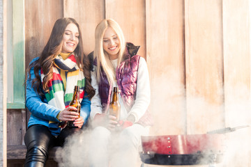 smiling women with beer in hands looking at barbecue