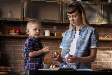 Young woman with her little brother painting Easter eggs in the kitchen