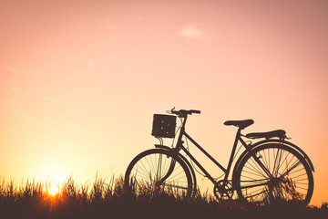 Fototapeta na wymiar Silhouette of old bicycle on grass with the sky sunset, color of vintage tone and soft focus concept journey