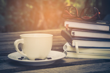 eyeglasses on book with hot coffee cup on nature background, vintage filter. learning concept and reading.