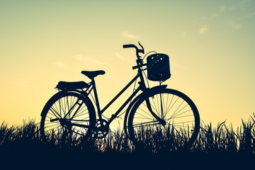Obraz premium Silhouette of old bicycle on grass with the sky sunset, color of vintage tone and soft focus concept journey