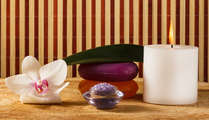 White orchid flower, candle, soap and sea salt for spa procedures on wooden background