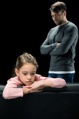 Fototapeta na wymiar Serious father with crossed arms looking at upset little daughter on black, family problems concept