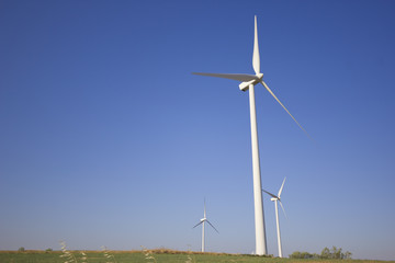 View of windmills towers from the ground with a cloudless blue sky.