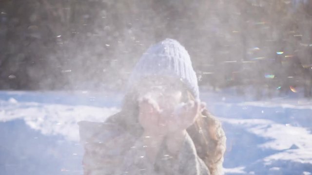 Girl in winter forest fun. Brunette blows snow from her palms and rejoices.