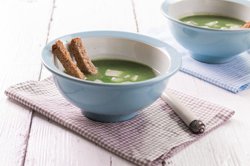 Fresh homemade cream of spinach soup in rustic bowls, homemade croutons on wooden table