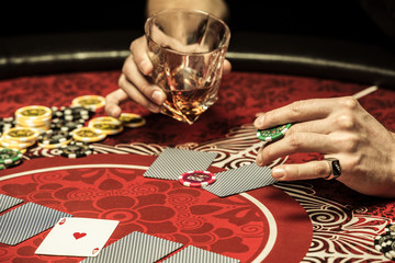 Close-up partial view of man holding glass of whisky and poker chip at table