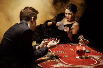 Elegant young woman lying on poker table and playing poker with man in suit