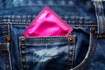 Pink condom in the pocket of blue jeans