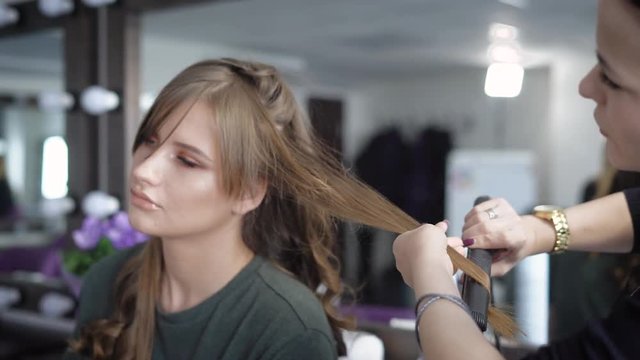 Hairdressing salon. The specialist in hair stacks the girl on a party. The hairdresser does ringlets by means of the special curling iron.