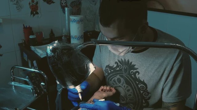 Tattoo Master does tattoo on woman's hand