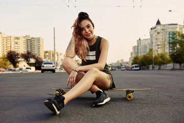 Beautiful young girl with tattoos sits on longboard in sunny weather © diignat