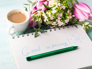 Wishing good morning hand written on notebook page and cup of coffee flowers. Spring summer...