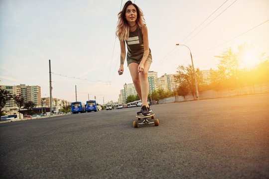 Beautiful young girl with tattoos riding on his longboard on the road in the city in sunny weather. Extreme sports