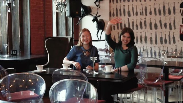 two missing girls wait for the friend sitting in the cafe during sunny day, and call up, waving hands when see she come after a long separation