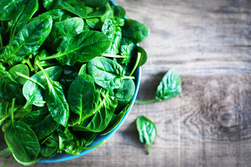 Fresh green baby spinach leaves in a bowl on a rustic wooden table close up..