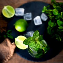 Fresh mojito drink with lime and mint in a glass on black stone board and wooden rustic table.