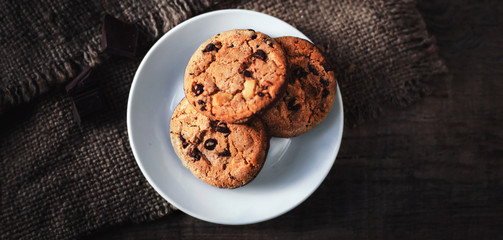 Chocolate chip cookies on white plate dark old wooden table with place for text.,  freshly baked. Selective Focus with Copy space..