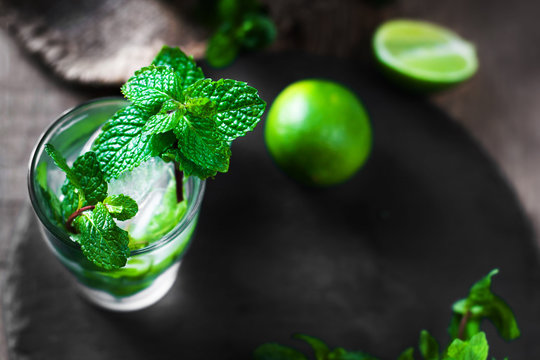 Fresh mojito drink with lime and mint in a glass on black stone board and wooden rustic table.