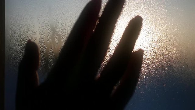 female hand in the foreground against a background of beautiful water drops on the glass, trying to pat the sun touch the sunset. 1920x1080