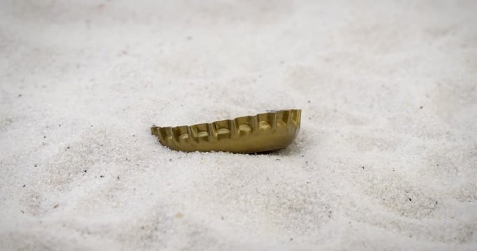 Concept for pollution of environment with beer cap slowly rotating on white sand beach
