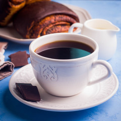 Homemade pastry with poppy seeds for breakfast icing chocolate on white plate with cup of coffee and milk on blue table background. copy space. 