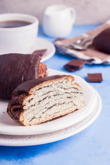 Homemade pastry with poppy seeds for breakfast icing chocolate on white plate with cup of coffee and milk on blue table background. copy space. 