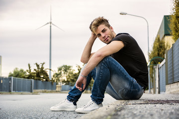 Attractive smiling man sitting by city street looking at camera