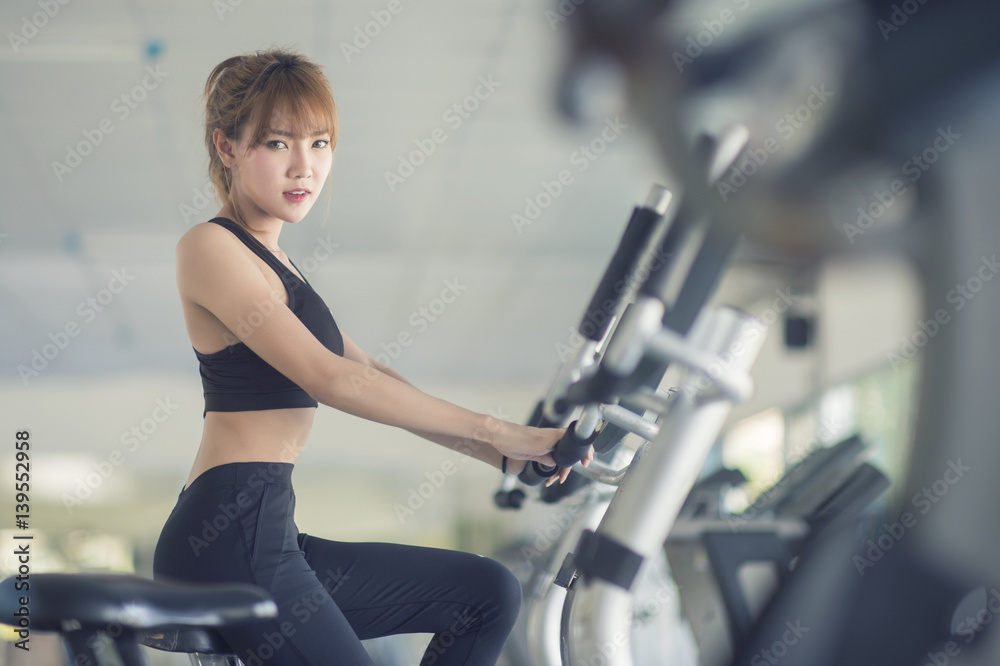 Wall mural sexy woman waer sport bar riding stationary bicycle in health club gym