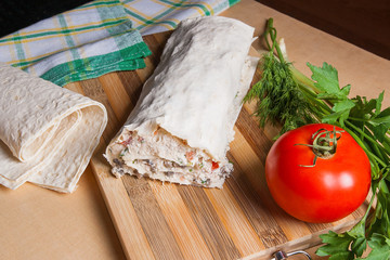 Pita bread or lavash wrapped with cottage cheese or curd, chicken, tomatoes and herbs - dill, onion, parsley on cutting board..