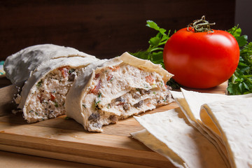 Pieces of cutted pita bread or lavash roll with cottage cheese or curd, chicken, tomatoes and herbs - dill, onion, parsley with intige knife on cutting board..