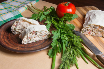 Two pieces of pita bread or lavash roll with cottage cheese or curd, chicken, tomatoes and herbs - dill, onion, parsley on brown clay plate..