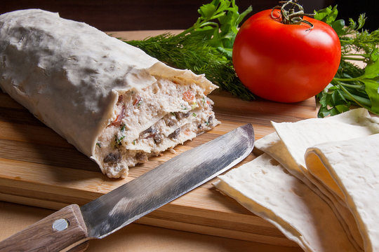 Pita bread or lavash wrapped with cottage cheese or curd, chicken, tomatoes and herbs - dill, onion, parsley. Lavash roll with vintage knife on cutting board.