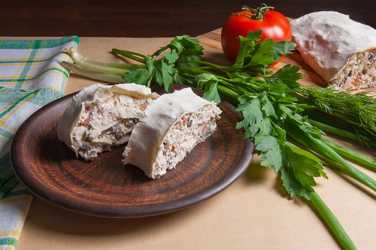Two pieces of pita bread or lavash roll with cottage cheese or curd, chicken, tomatoes and herbs - dill, onion, parsley on brown clay plate..