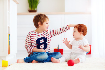 cheerful senior kid playing with his junior toddler brother at home