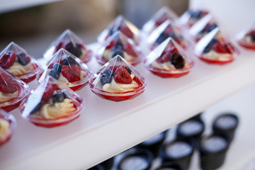 monoporzioni a forma di prisma con dolcetti ai frutti  di bosco sopra su un espositore bianco - altri dolci sullo sfondo
