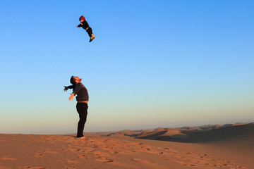Vater wirft fröhlich seinen Sohn in die Luft und fängt ihn wieder auf, Namib Wüste
