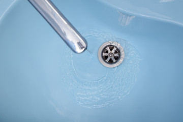 Water flows from the tap in a blue washbasin. The liquid pours out, swirling, in the open plug