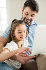 portrait of father teaching daughter how to use laptop