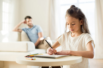 portrait of focused daughter drawing picture with father behind