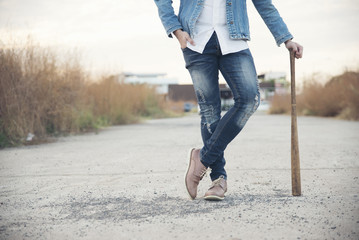 Closed up of legs's smart man wearing blue jeans and jacket standing on the cement patio and holding a baseball bat.