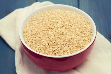 raw rice in red bowl on wooden background