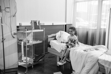black and white photo of upset girl with teddy bear sitting on hospital bed