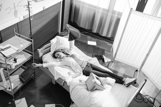 High Angle View Of Doctor With X-ray Picture Lying On Hospital Bed, Black And White Photo