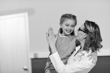 Smiling doctor and happy little girl patient looking at each other, black and white photo