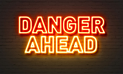 Danger ahead neon sign on brick wall background.