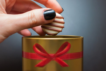 mano che tiene caramella di cioccolato della donna, tirato fuori da una scatola d'oro rotonda con un fiocco rosso su sfondo nero
