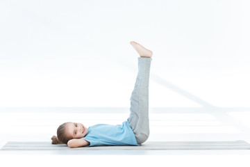 Cute little girl exercising on yoga mat and smiling at camera